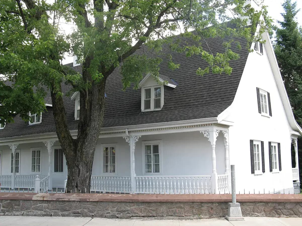 Maison blanche à galerie sous un grand arbre, au Québec